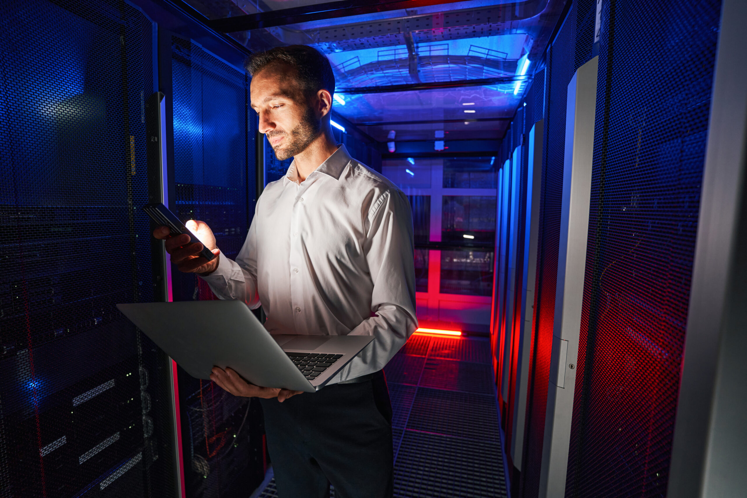 Man technician doing maintenance work for dedicated server in data colocation center with laptop and analyzer device